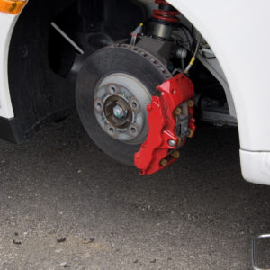 Closeup detail of the wheel assembly and six piston calipers on a modern sports car braking system. The rim is removed showing the front rotor and caliper.